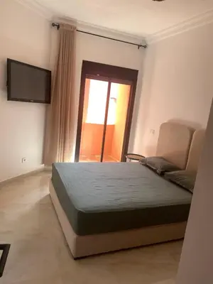 a bedroom with a bed and a tv and a window at Bel Appartement Vue Piscine in Marrakech