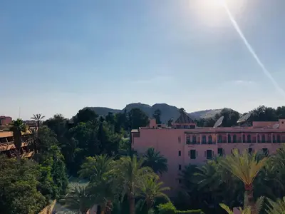 a large pink building with palm trees and mountains in the background at APPARTEMENT MODERNE AU CENTRE m in Marrakech