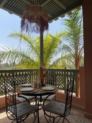 a table and chairs on a patio with palm trees at 2 bedroom palmeraie, pools & 3 terraces in Marrakech