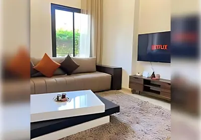 a living room with a couch and a tv at Ehden Properties - Appt spacieux dans la prestigieuse River Palm Marrakech in Marrakech