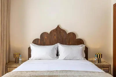 a bed with a wooden headboard and white pillows at Charme Marrakchi - Piscine, Jardin & Espace Sport in Marrakech