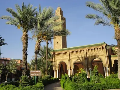 a building with palm trees and a clock tower at Riad Marrakech - Piscine -Wifi- résidence qarya essyahia in Marrakech
