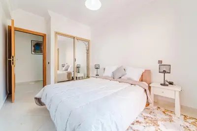 a white bedroom with a large bed and a mirror at Appartement Malika Gueliz in Marrakech