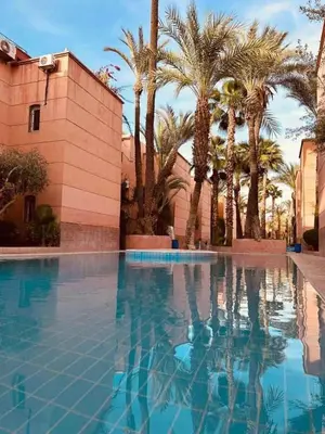 a swimming pool with palm trees and a building at Riad Al Hanaa in Marrakech