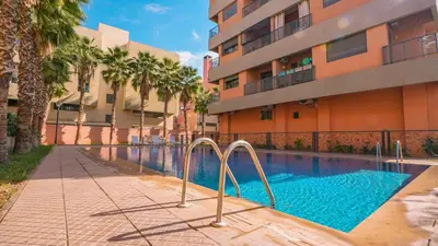 a swimming pool in front of a building with palm trees at Appartement chaleureux agréable pour des vacances en famille in Marrakech