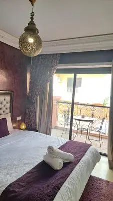 a bedroom with a bed and a balcony with a table at Appartement tres aimable in Marrakech