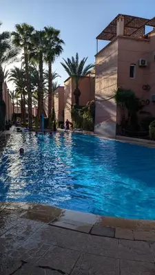 a large blue swimming pool with palm trees and buildings at Apartment lhaja in Marrakech