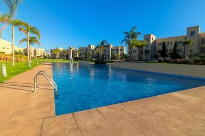 a swimming pool in a resort with palm trees and buildings at Appartement Cosy Prestigia 2 Chambres in Marrakech
