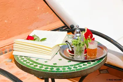 a table with a book and a drink and flowers on it at Riad Mounir in Marrakech