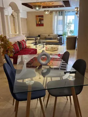 a living room with a glass table and blue chairs at Sofia Palmeraie Appartement in Marrakech