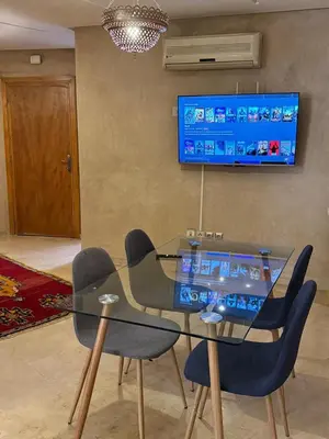 a glass table with chairs and a television on a wall at Sofia Palmeraie Appartement in Marrakech