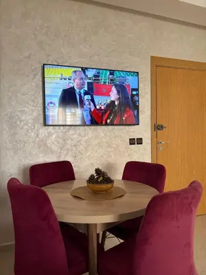 a dining room table with a tv on the wall at Charmant appartement familial in Marrakech