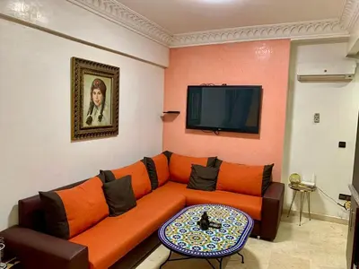 a living room with an orange couch and a tv at Appartement Miramas 2 E2 in Marrakech