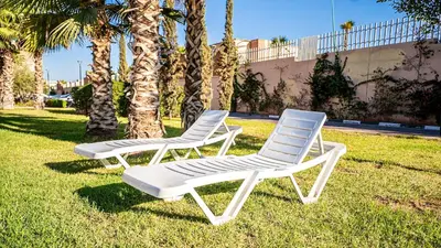 two white chairs sitting in the grass near palm trees at Résidence Coralia, 10 minutes de Guéliz, place Jemaa El Fna in Marrakech