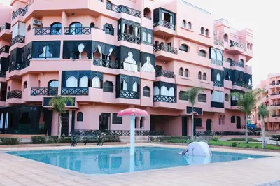 a pink apartment building with a swimming pool and an umbrella at Charming apartment in a tourist village Premium village in Marrakech