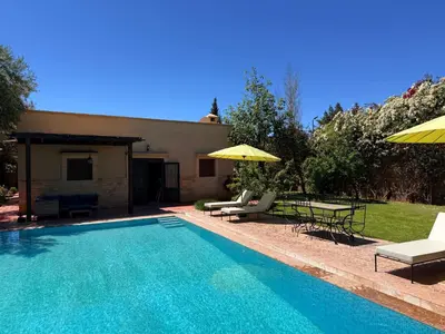 a swimming pool with chairs and umbrellas next to a house at DAR ENNAGA - Havre de paix, avec piscine chauffée , à 10 minutes de Marrakech in Marrakech