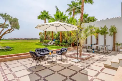 a patio with a table and chairs and an umbrella at M REVASION villa 5 chambres front de golf Petit déjeuner petit ménage et Tranfert aéroport inclus in Marrakech
