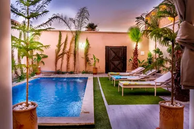 a courtyard with a pool with lounge chairs and palm trees at Villa loujain in Marrakech