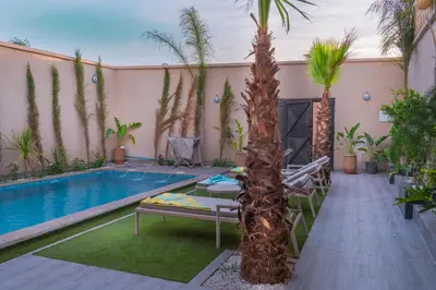 a pool with a palm tree next to a building at Villa loujain in Marrakech