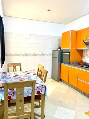 a kitchen with a table and a kitchen with orange cabinets at Magnifique F3 au Riad Arfoud avec piscine in Marrakech