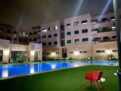a hotel pool with a red chair in front of a building at Magnifique F3 au Riad Arfoud avec piscine in Marrakech