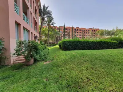 a grassy yard next to a pink building with bushes at Apartment with pool and garden in Marrakech