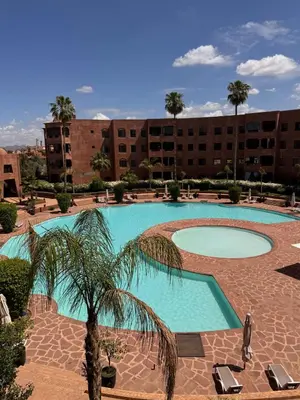 a large swimming pool with a palm tree in front of a building at Superbe appartement Marrakech Piscine Wifi Climatisation in Marrakech