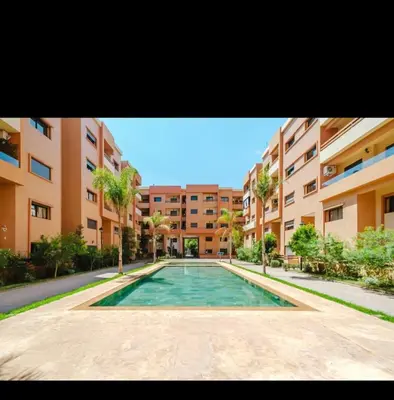 a swimming pool in front of a building with palm trees at Appartement a hivernage in Marrakech