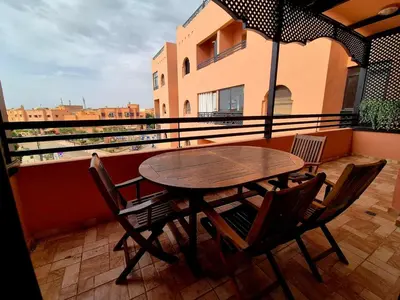 a table and chairs on a balcony with an umbrella at Comfortable poolside apartment near city center in Marrakech