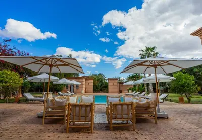 a patio with chairs and umbrellas and a pool at Villa des SONGES in Marrakech