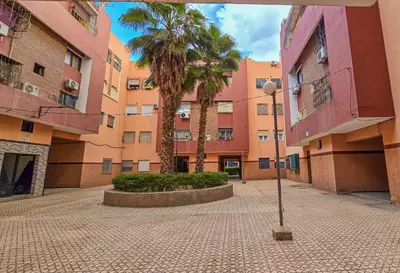 a courtyard with palm trees in front of a building at Appartement Chic et Confortable, Netflix, PS4 & Wi-Fi Centre Marrakech in Marrakech