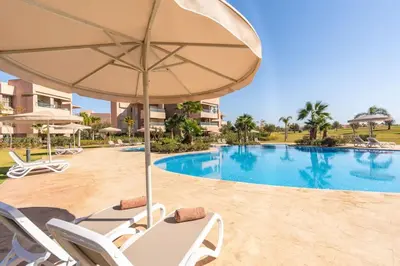 a swimming pool with chairs and an umbrella and a pool at Vue Piscine et Golf Luxueux rez de jardin in Marrakech