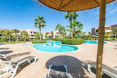 a swimming pool with chairs and an umbrella at Spacious Apartment, Golf & Pool in Marrakech