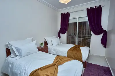 a bedroom with two beds and a window with purple curtains at appartement majorelle in Marrakech