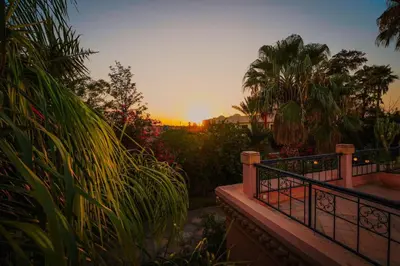 a sunset over a garden with palm trees and a fence at La Villa Wassim in Marrakech