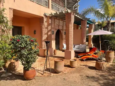 a house with a patio with a chair and an umbrella at Appartement les jardins de la Palmeraie III in Marrakech