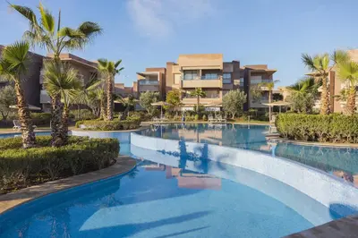 a swimming pool with palm trees in front of a building at Beautiful 3 bedroom apartment for 6 people Prestigia Golf Saphir in Marrakech