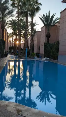 a blue swimming pool with palm trees in the background at Atelier des Reeves in Marrakech