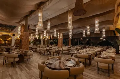 a dining room with tables and chairs and chandeliers at NOMMOS Beach RESORT & POOL CLUB in Marrakech
