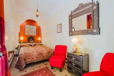 a bedroom with a bed and a red chair at Riad Alzira Jardin Secret Au coeur De La Medina in Marrakech