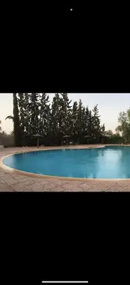a large blue swimming pool with trees in the background at Élégance & fraîcheur Appart avec piscine in Marrakech