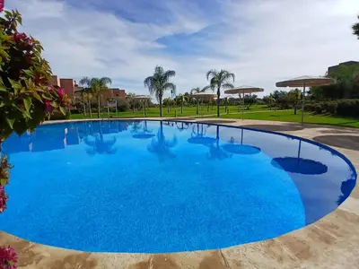 a large swimming pool with blue water at Appartement Prestigia Marrakech Maroc Golf Piscine in Marrakech