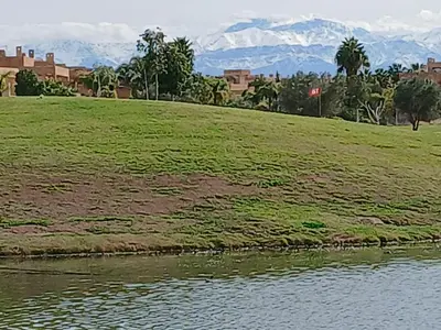 a grassy field with mountains in the background and a body of water at Appartement Prestigia Marrakech Maroc Golf Piscine in Marrakech