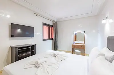 a white bedroom with a bed and a television at AliZ Appartement 2 chambres avec piscine, Majorelle in Marrakech
