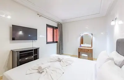 a white bedroom with a bed and a tv at AliZ Appartement 2 chambres avec piscine, Majorelle in Marrakech
