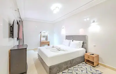 a white bedroom with a bed and a television at AliZ Appartement 2 chambres avec piscine, Majorelle in Marrakech