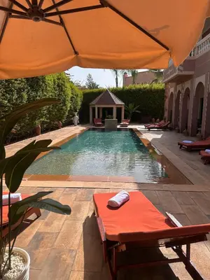 a swimming pool with an orange umbrella and a table at Villa luxueuse marrakech in Marrakech