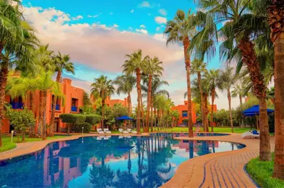a swimming pool with palm trees and buildings at Riador in Marrakech