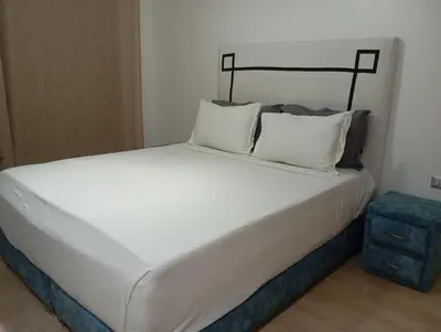 a large white bed with two pillows and a blue stool at Appartement prestigia golf in Marrakech
