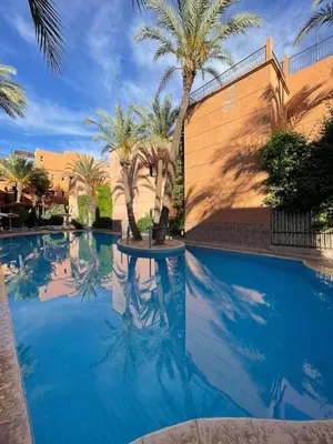 a swimming pool with palm trees and a building at Al Qaria Syahia Duplex Moufid in Marrakech